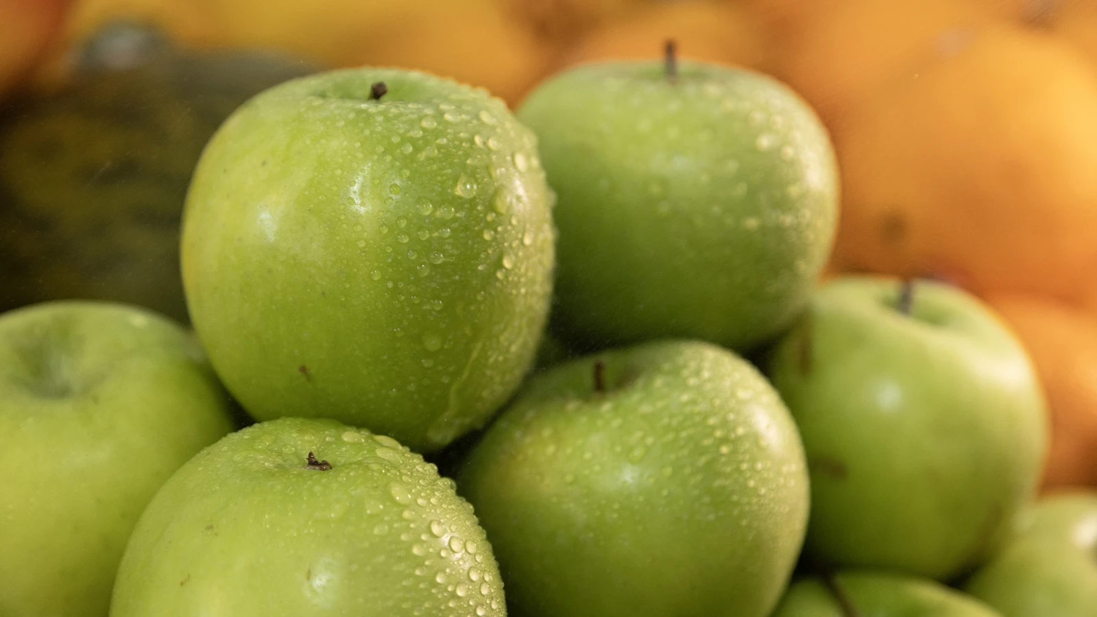 Maçãs verdes com gotas de água na bancada do hortifrúti do Megamix